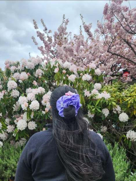 Person with a purple hair accessory standing in front of flowering bushes